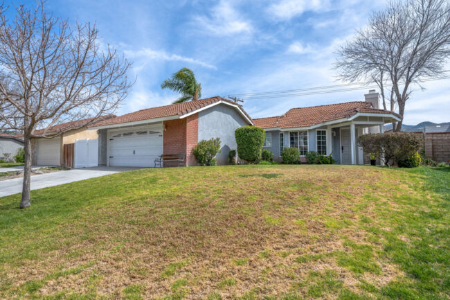 Blue and red brick house on a small grass hill.