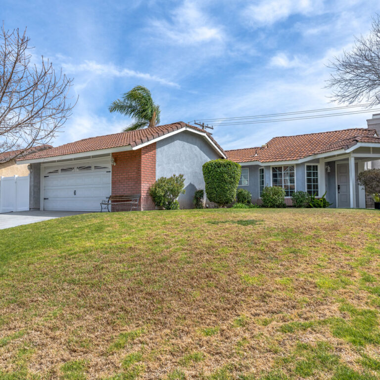 Blue and red brick house on a small grass hill.